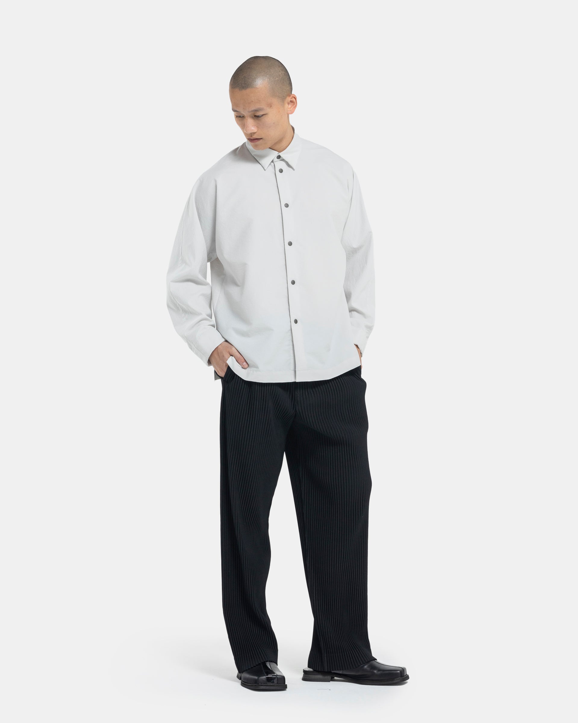 Male model wearing black Homme Plissé Issey Miyake pants on white background