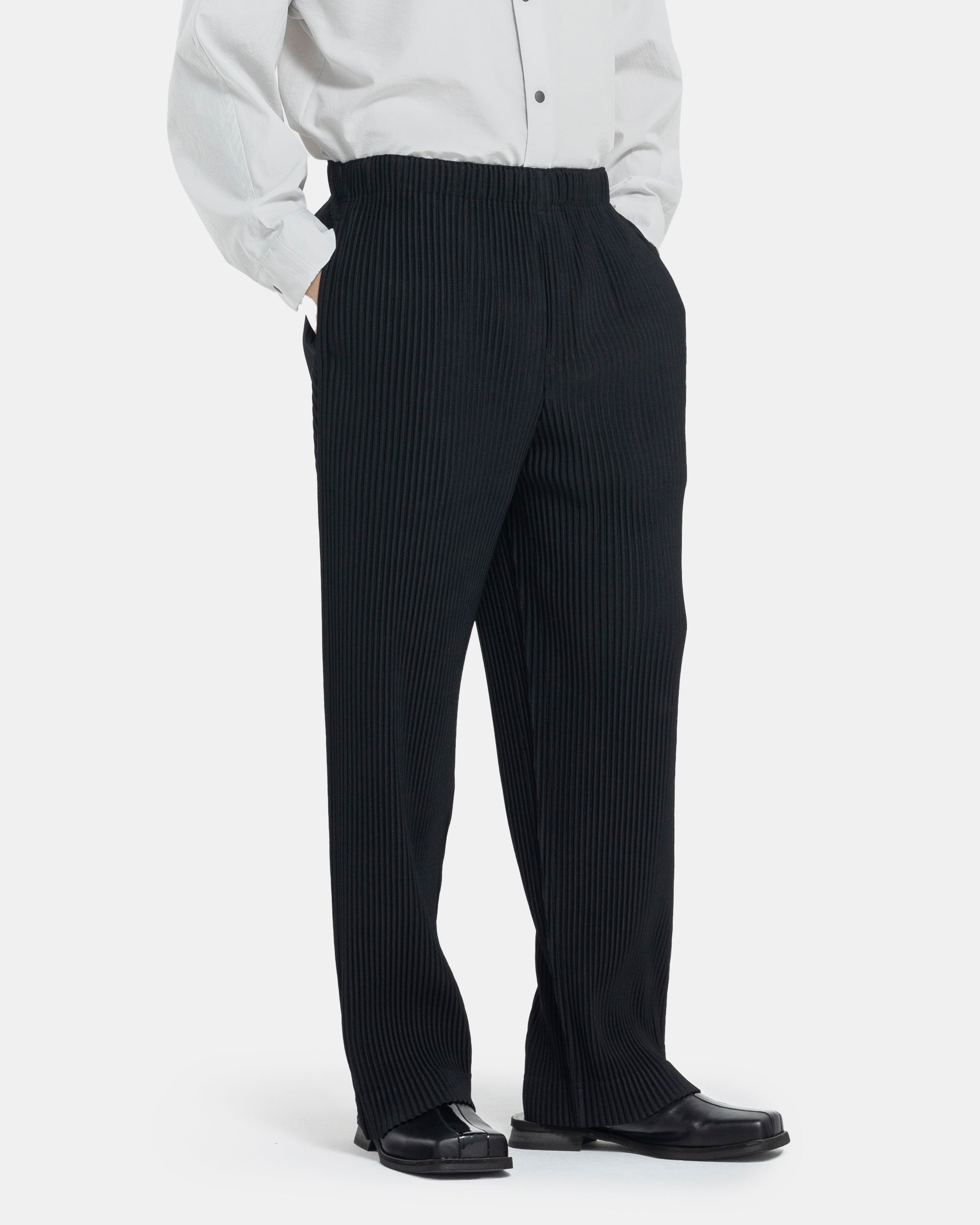 Male model wearing black Homme Plissé Issey Miyake pants on white background