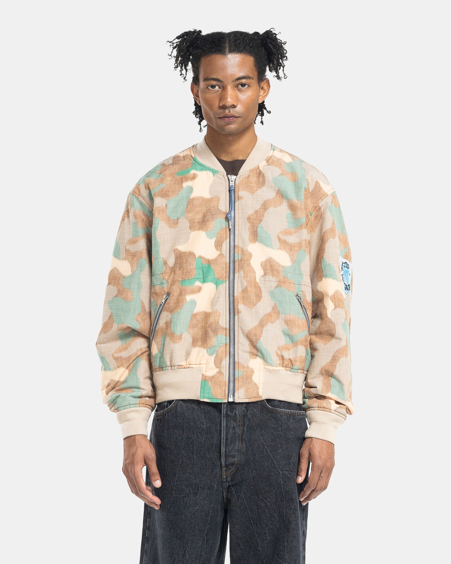 Model wearing Acne Studios Camo Bomber Jacket in Orange & Green on the white background