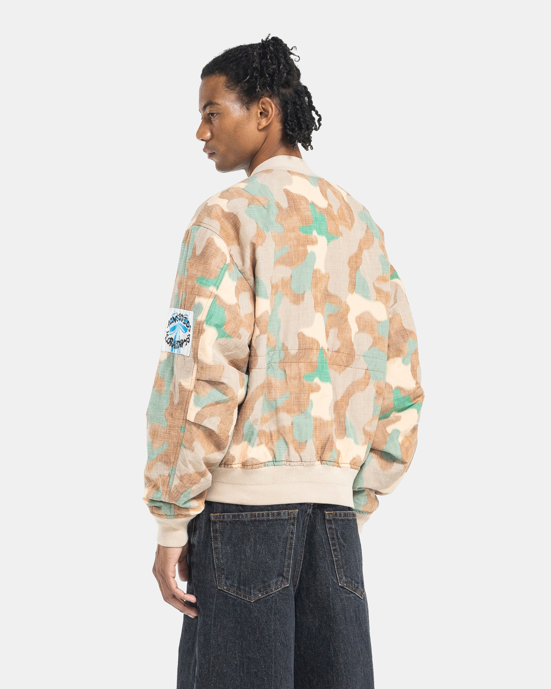 Model wearing Acne Studios Camo Bomber Jacket in Orange & Green on the white background